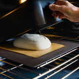 Lifting the baking shell to reveal the dough resting on the bread steel in the oven.